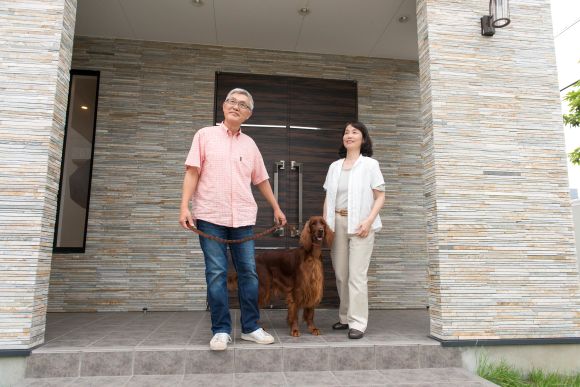 犬と一緒に家を出る夫婦の写真
